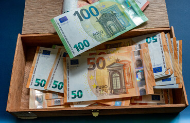 Durcheinander von verschiedene Euro Banknoten,fünfzig Euro Schein und 100 Euro Schein,in einer alten Zigarrenkiste vor blauen Hintergrund