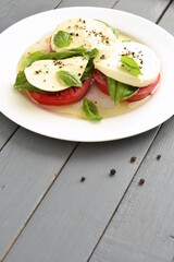 Caprese salad of tomato, mozzarella, basil on gray wooden background . Italian food, vertical,  copy space