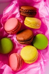 multicolored macarons cakes on a cardboard box in a pink paper background