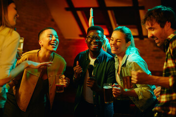 Young carefree friends having fun and singing karaoke while having a party at nightclub.