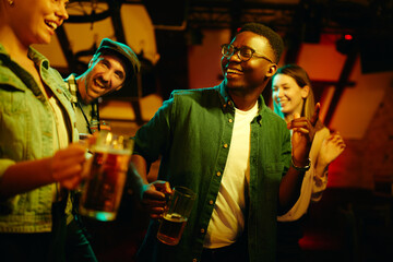 Happy black man dancing with his friends and having fun in a bar at night.