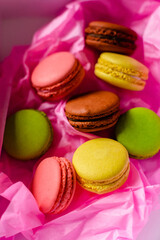 multicolored macarons cakes on a cardboard box in a pink paper background
