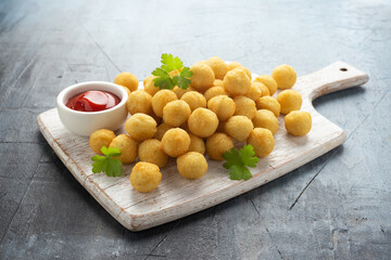 Crispy potato balls with ketchup on white wooden board