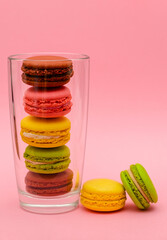 several color macaron cakes in a glass cup on a pink background