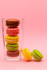 several color macaron cakes in a glass cup on a pink background
