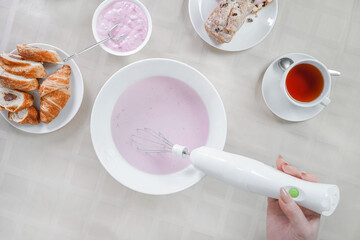 woman preparing dessert top view. female hand holds mixer and whips cream on white background