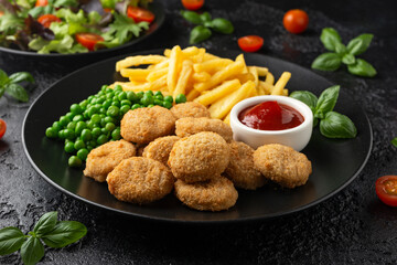 Fried crispy chicken nuggets with ketchup, french fries and green peas in black plate