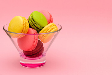 several color macaron cakes in a glass vase on a pink background