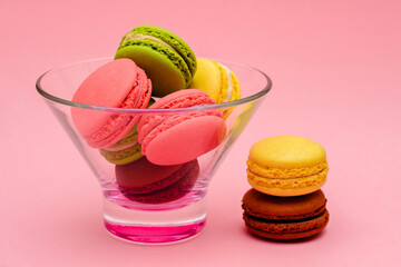 several multicolor macaron cakes in a glass vase on a pink background