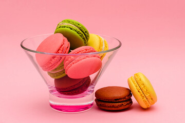 several color macaron cakes in a glass vase on a pink background