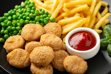 Fried crispy chicken nuggets with ketchup, french fries and green peas in black plate