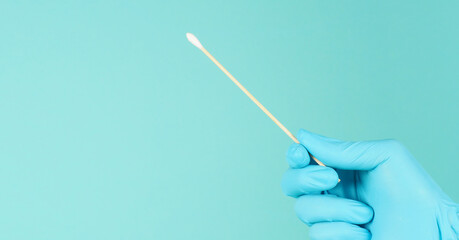 One Cotton stick for swab test in hand with blue medical gloves or latex glove on mint green or Tiffany Blue background.covid-19 concept