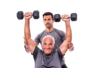 Gordijnen Elderly male client exercising with a fitness trainer, lifts dumbbells. On a white isolated background. © sergojpg