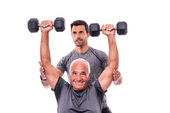 Elderly male client exercising with a fitness trainer, lifts dumbbells. On a white isolated background.