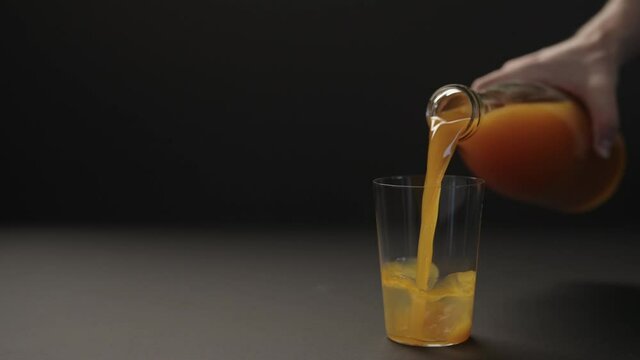 Slow motion man hand pour mango juice into tumbler glass on black paper background with copy space