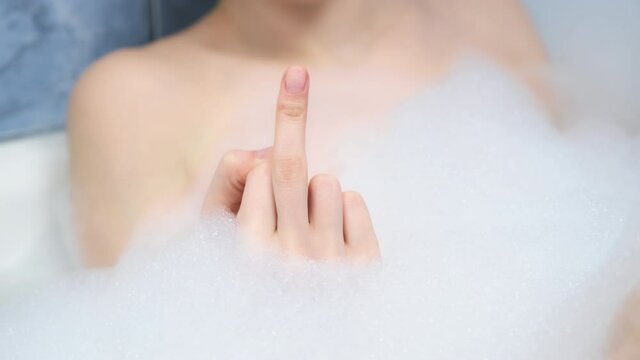 Fuck you sign by woman hand in foam in bath, middle finger sign, closeup view. A sign of aggression, indifference and rejection, rudeness and boorishness.