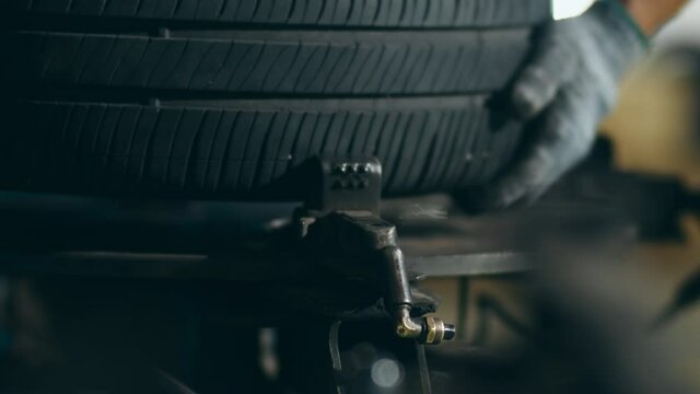 Professional car mechanic changing a car tire on lifted automobile at repair service station. Wheel alignment work at workshop night. Skillful Asian guy in uniform fixing car. Car service repair.