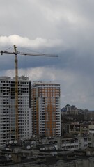Fototapeta na wymiar Construction site of unfinished multistory building with crane jib at overcast sky background. Under construction cityscape with rooftops and cloudscape. Vertical shot