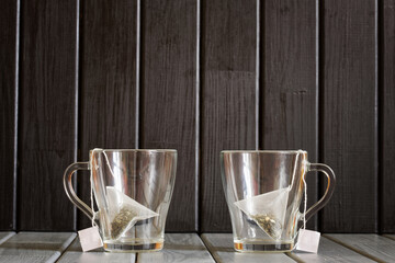 Two transparent mugs with pyramid tea bags stand on a wooden vintage table. Element of a roadside...