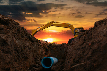 Crawler excavator is digging in the construction site pipeline work on sunset sky background - obrazy, fototapety, plakaty