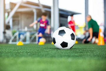 Selective focus to soccer ball on green artificial turf with blurry soccer team is training. Sport background. Soccer background.