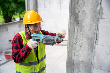 tiler using electric impact drill to drilling cement wall at unfinished house construction