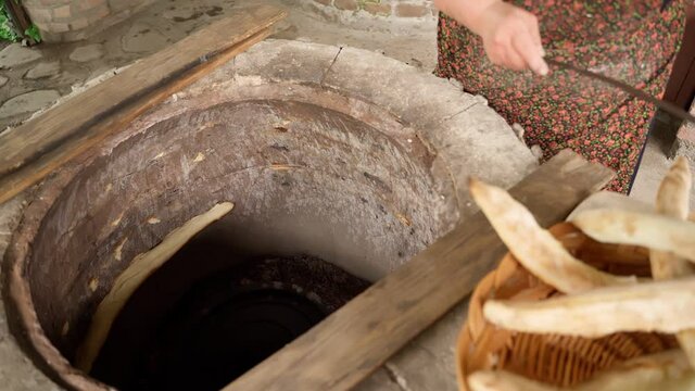  Woman cooking at outside kitchen traditional Georgian flat bread Shotis puri in radiant heat cooking oven with fire. Video footage