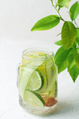 Glass mug with handle with refreshing detox lemonade with sliced lime, lemon, cucumbers and red orange on white table. 