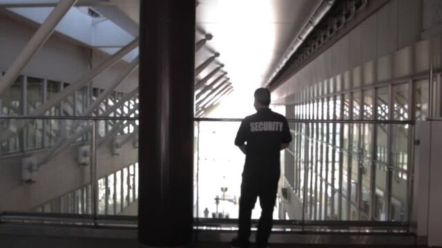 A rearview of a security guard in uniform patrolling in a commercial building.