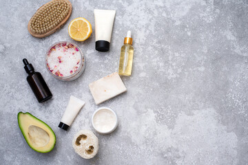 Fototapeta na wymiar Organic spa cosmetics products, lemon, avocado, serum and cream, sea salt, massage brush on gray marble table top. Copy space