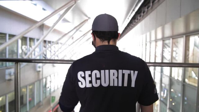 A rearview of a security guard in uniform patrolling in a commercial building.