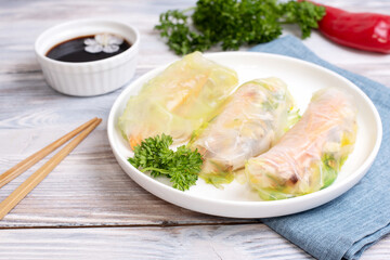 Fresh spring rolls on a white plate with textiles and soy sauce on a white wooden background, vietnamese cuisine.