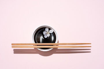Soy sauce, teriyaki in white bowl with chopsticks and cherry blossom on pink background in bright sunlight.