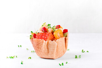 Fruit salad in waffle cup on white. Grapefruit, banana, kumquat, pear, apple, kiwi, cherry and microgreen mixed and served. Kids food