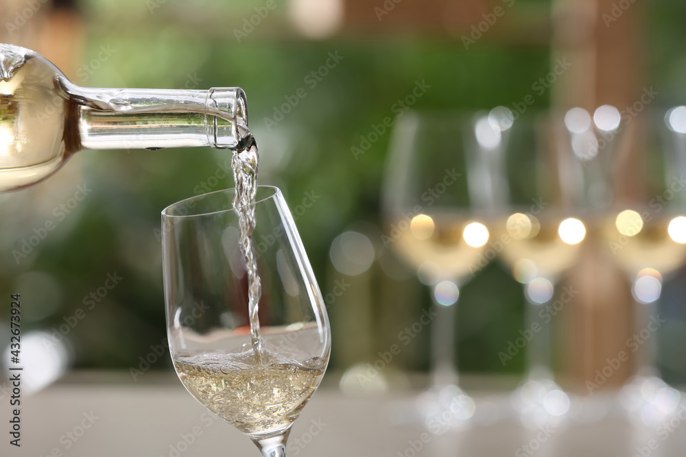 Poster Pouring white wine from bottle into glass on blurred background, closeup. Space for text