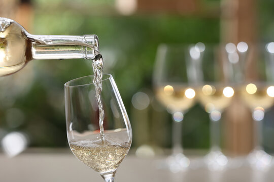 Pouring white wine from bottle into glass on blurred background, closeup. Space for text
