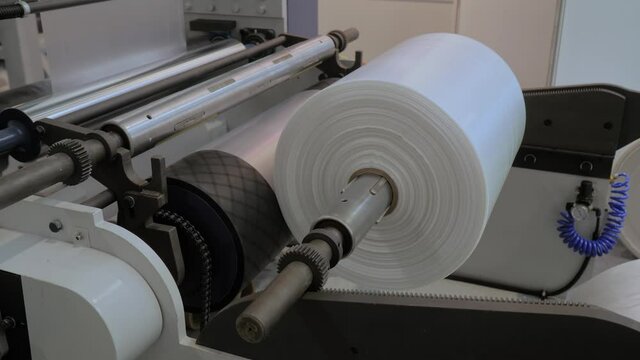 Moving roller with flat polyethylene transparent film - automatic plastic bag making machine at exhibition, trade show. Recycling, manufacturing, industry, automated technology equipment concept