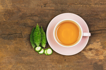 Bitter gourd or bitter melon tea in ceramic cup on wooden background, top view. Scientific name is...