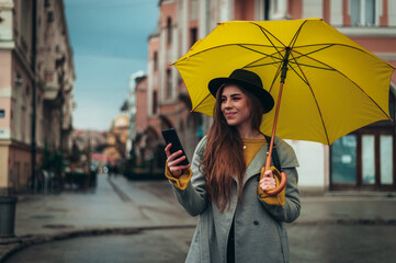 Woman using a smartphone while holding a yellow umbrella outside