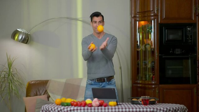 Wide shot portrait of cheerful Middle Eastern man juggling oranges at home in kitchen. Happy smiling young handsome chef posing indoors with healthful fruits. Healthy eating concept