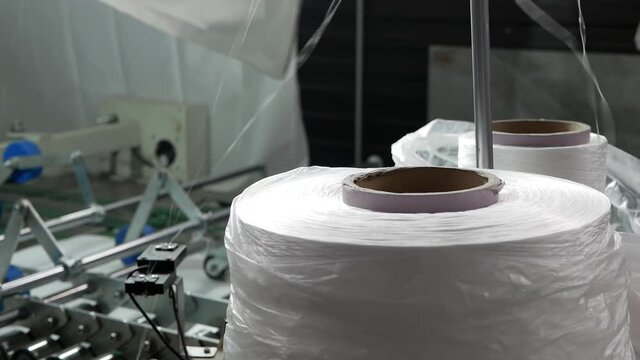Conveyor line for the production of bags for cereals. A large spool of thread is unwound on an industrial sewing machine. Enterprise for the production of containers, polyethylene bags, big bags.