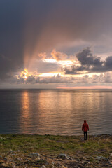man in red jacket standing on cliffs watching sunrise over ocean in Greystones Ireland
