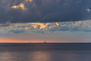a small boat on the horizon at sunrise with incredible clouds