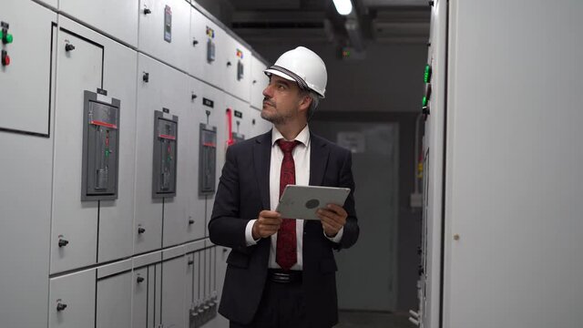 Industry Engineer manager using digital tablet checking information and safety system of Electrical switch gear cabinets with control panels at Industrial Manufacturing Factory. businessman inspecting