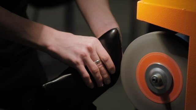 Close up: shoemaker, shoes master using automatic orange shoe polish machine tool for polishing black leather women footwear at workshop