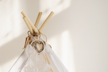 White fabric tepee top with decorative wood hearts and white feathers dream catcher with copy space.