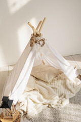 White fabric kids teepee and Native American decor in a children's room on a sunny day. © July P