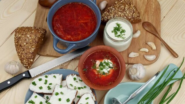 Russian and Ukrainian cuisine. Borscht with sour cream and spices, fresh herbs, garlic and pampushki. Beetroot soup in a blue bowl on a wooden board. Top view
