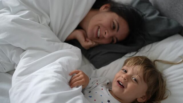 Baby toddler and mother playing hide and seek under bed comforter in morning wake up
