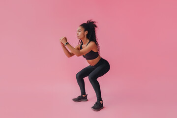 attractive black african american woman in black leggins fitness outfit on pink background